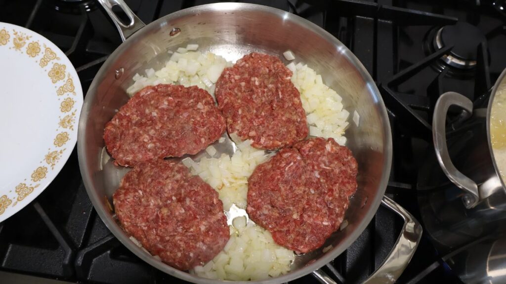 raw salisbury steak patties in skillet with onions