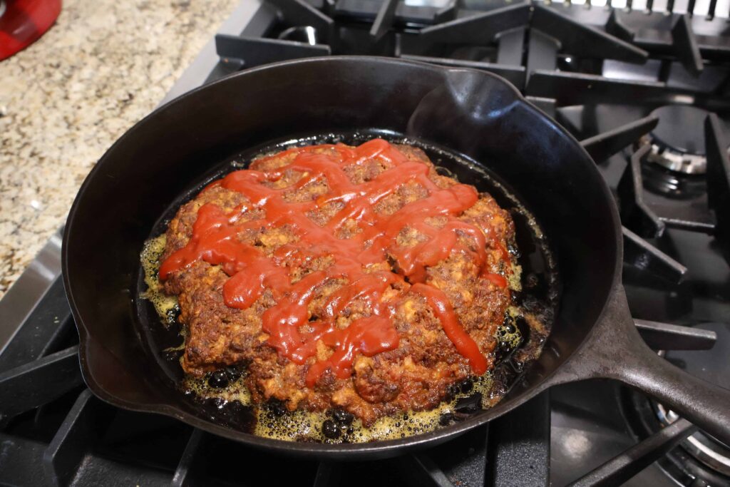 cooked meatloaf in cast iron with ketchup glaze on top