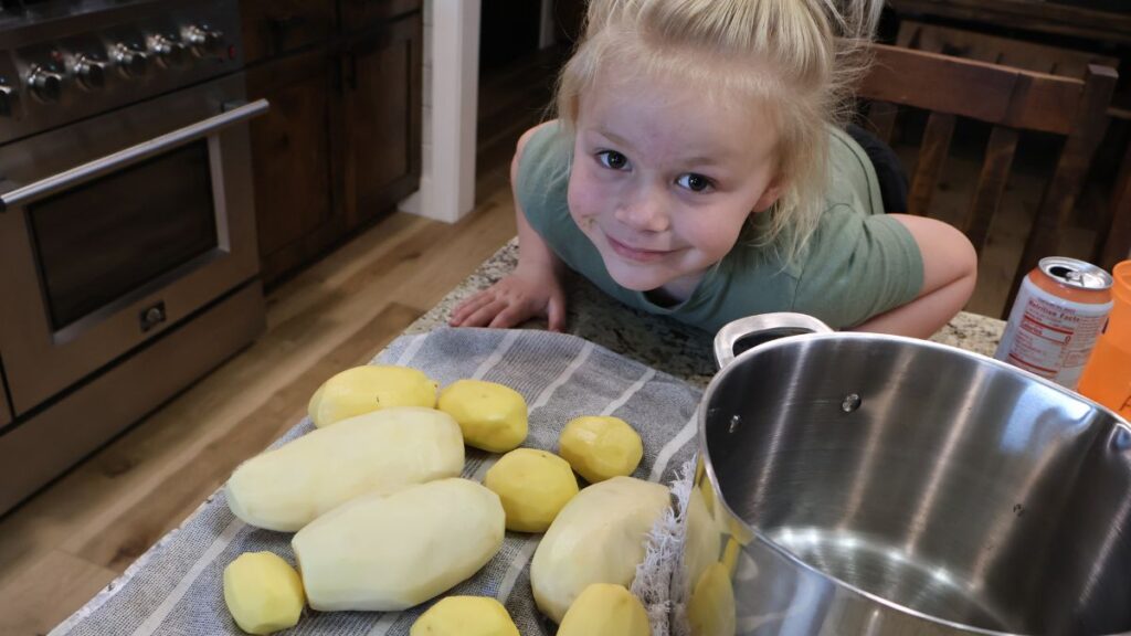 little girl posing by peeled potatoes and stock pot