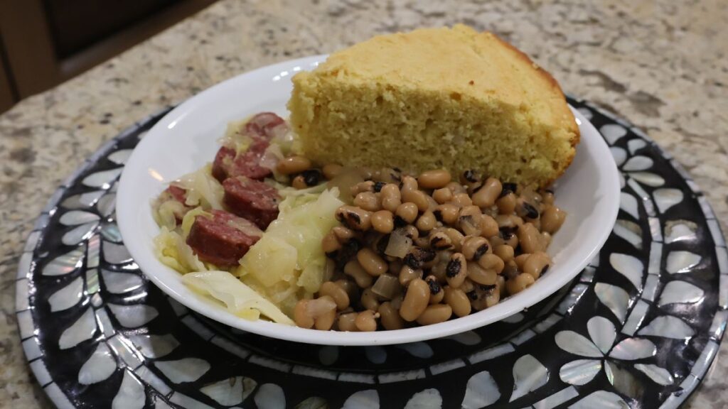 black eyed peas in large bowl with cabbage and cornbread