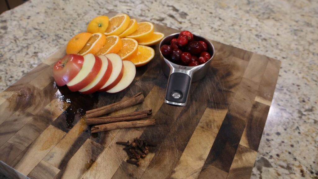 cut apples, cut oranges, cranberries, cinnamon, and cloves on cutting board
