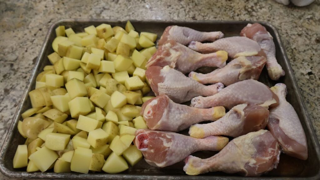 raw chicken legs and cut potatoes on sheet pan